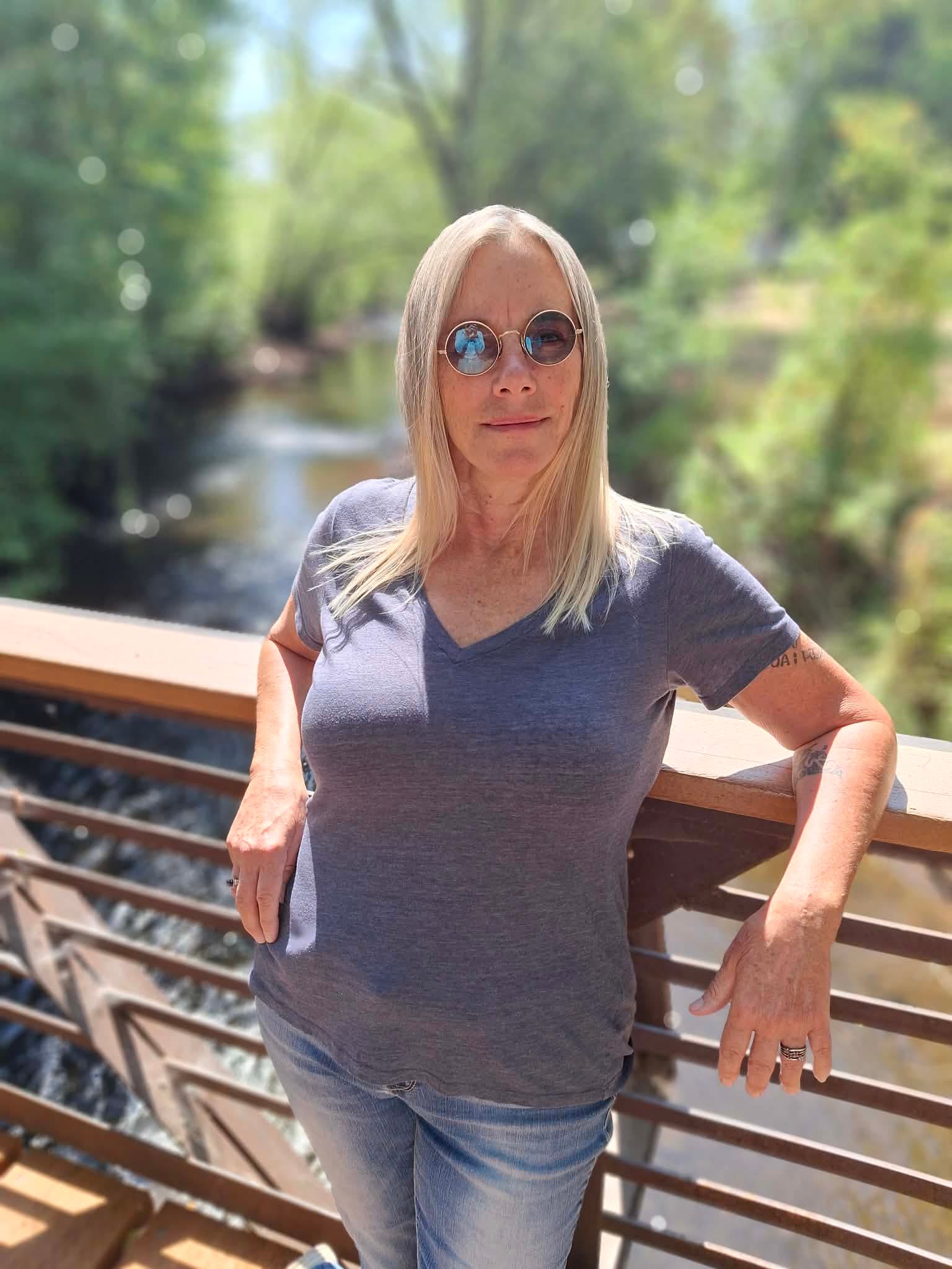 Elsa C White leaning on a railing above a creek, surrounded by trees.