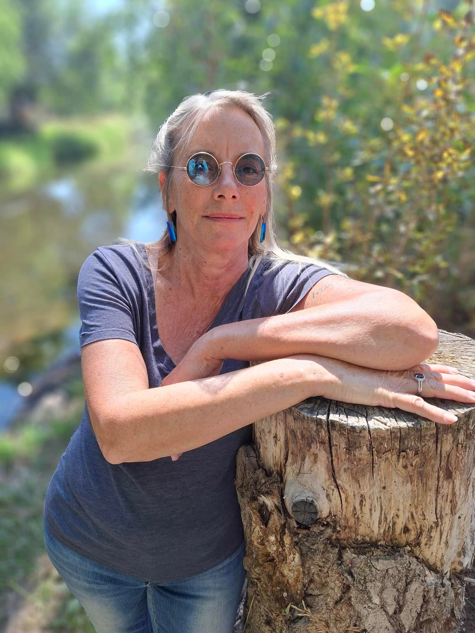 Elsa C White resting her arms on a tree stump outdoors.